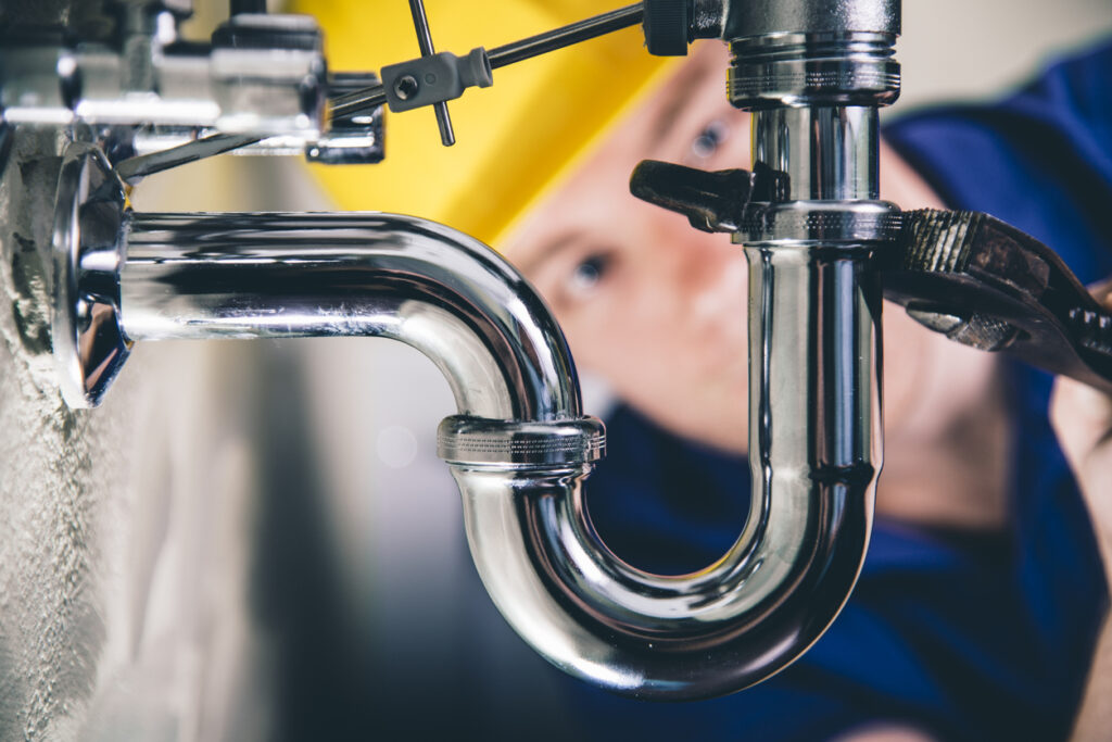 Buckhead Plumber fixing a drain with adjustable wrench. Focus on drain, plumber defocused in back.